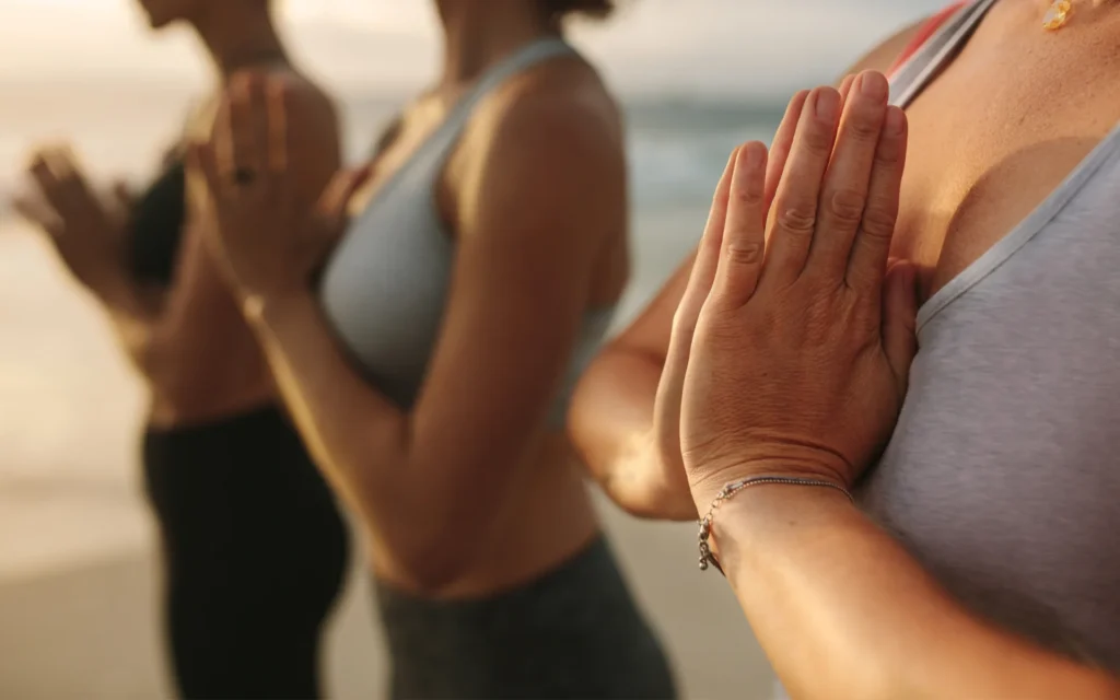 Women meditating on the beach at sunset, using mindfulness as a natural way to relieve stress and enhance physical and emotional well-being. A reflection of Azala Natura’s holistic approach to health.